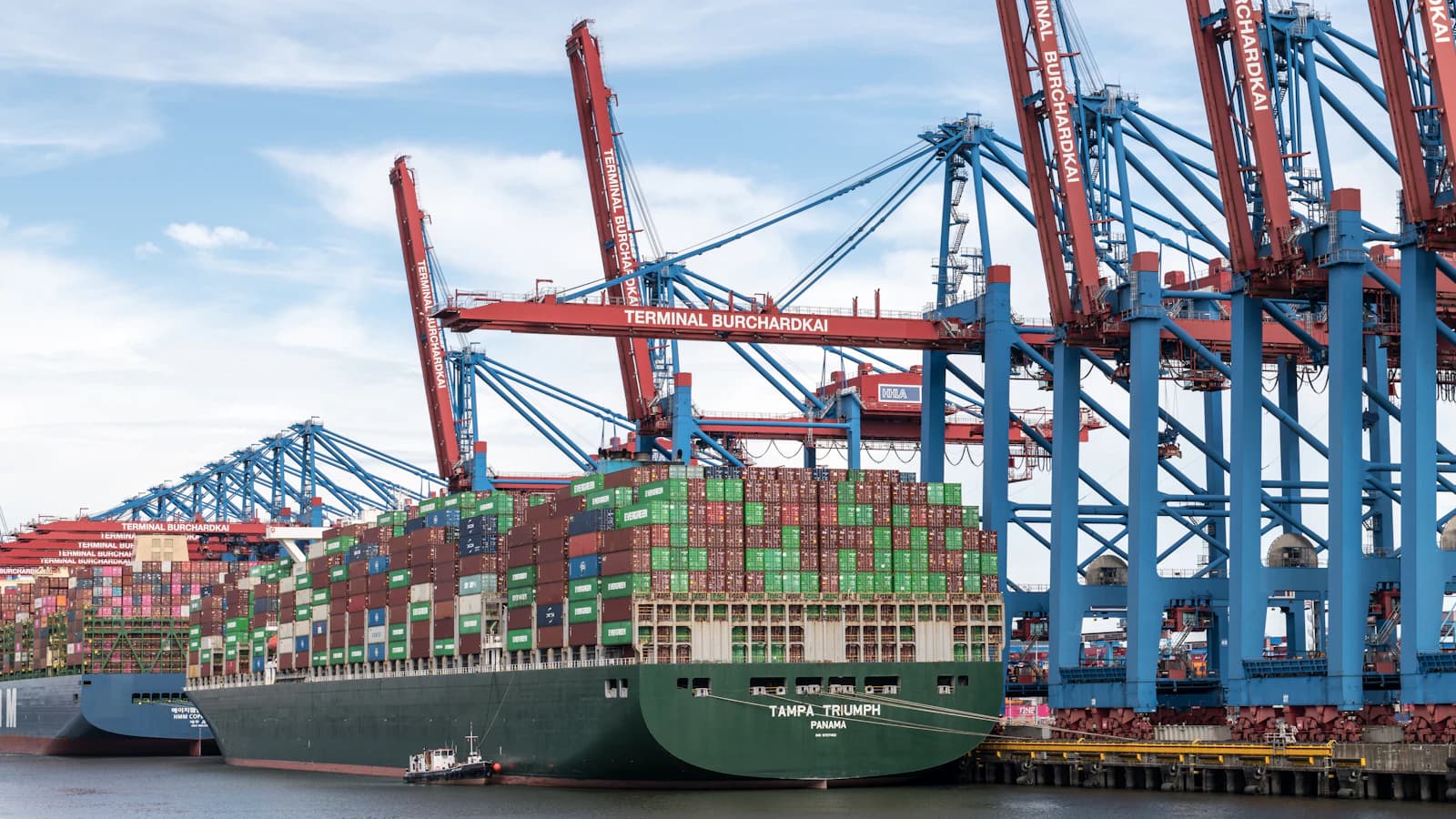 Container ship docked at a busy terminal under a row of gantry cranes