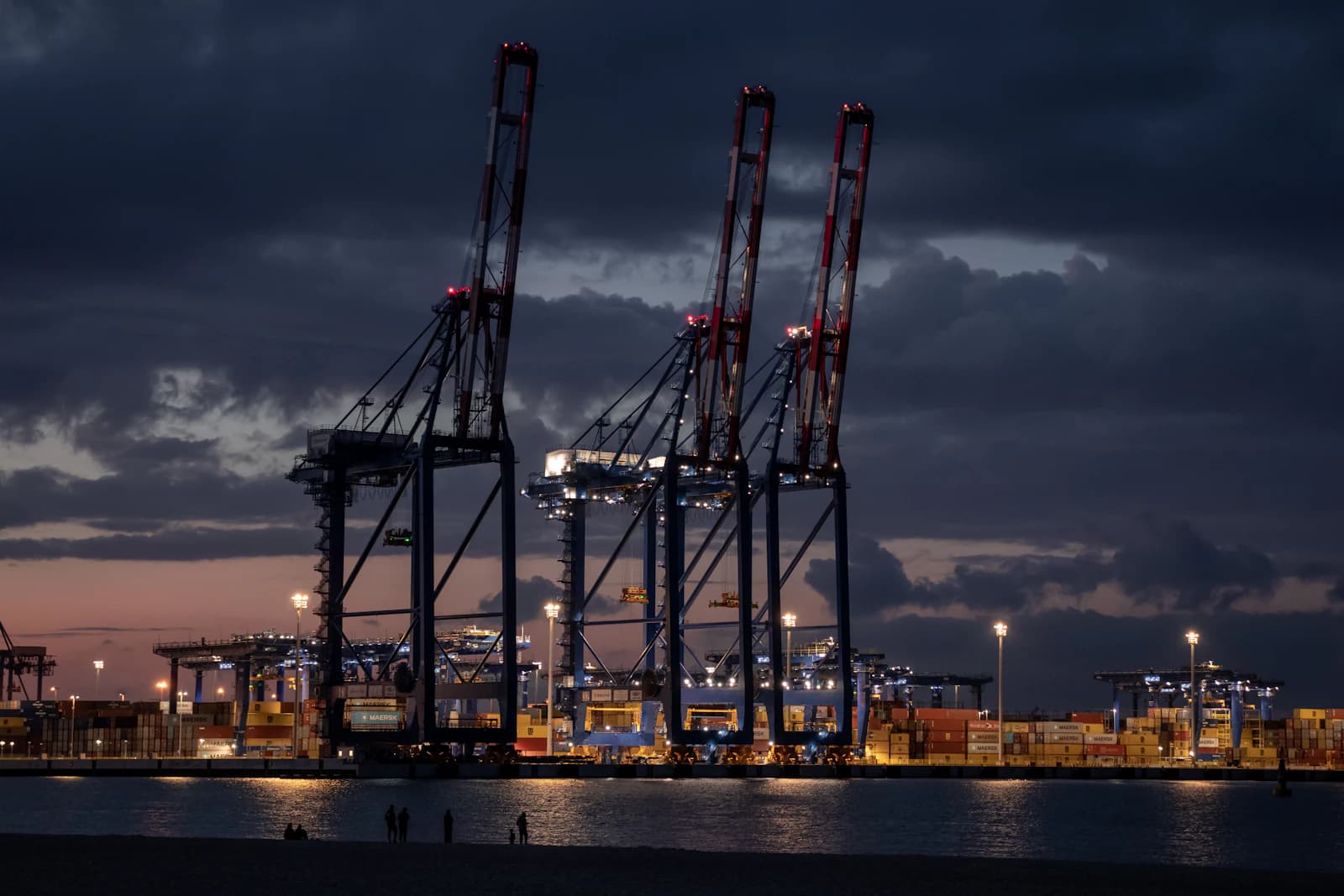 Harbour cranes at dusk with container rows lit along the quay