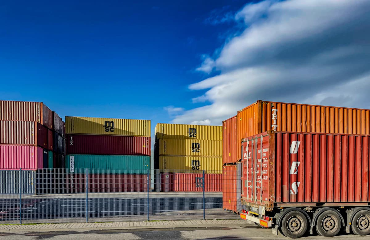Stacked shipping containers in a freight terminal with a truck passing